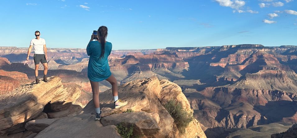 a woman takes a photo of a man standing atop a Grand Canyon National Park rock formation