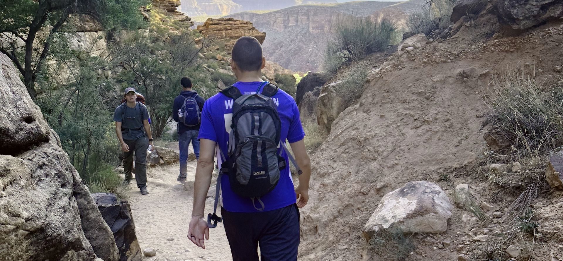 three men walk along a wooded Grand Canyon South Rim trail