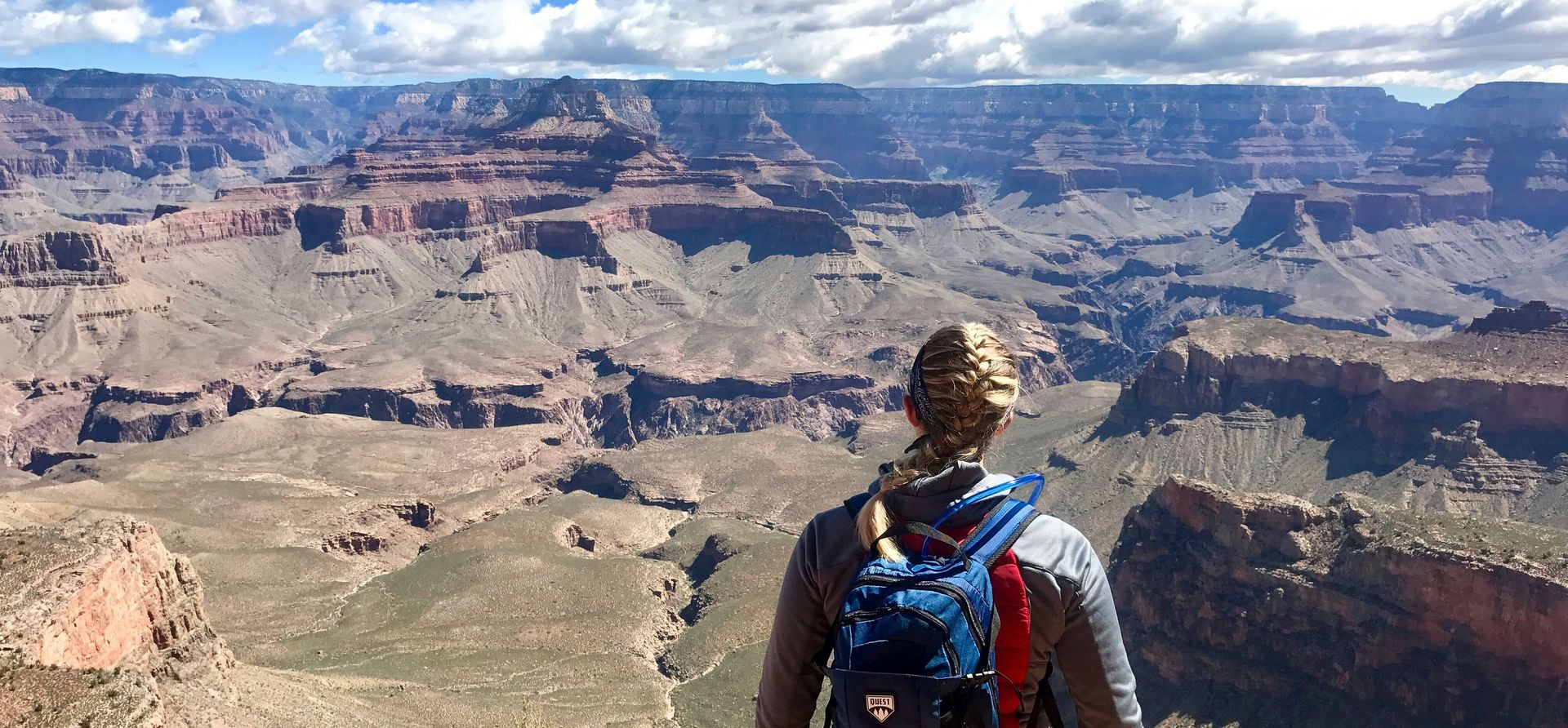 a woman wearing a backpack gazes out over a South Rim lookout point