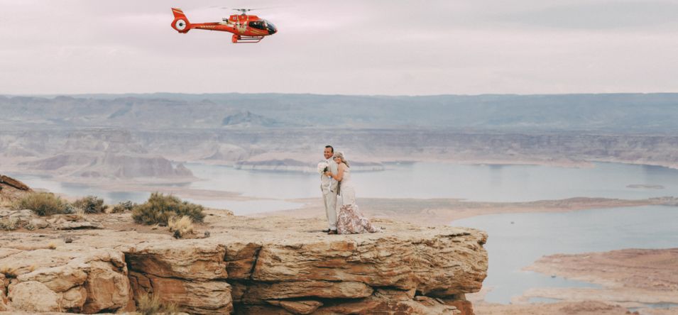 a wedding couple posing with a red helicopter flying in the background