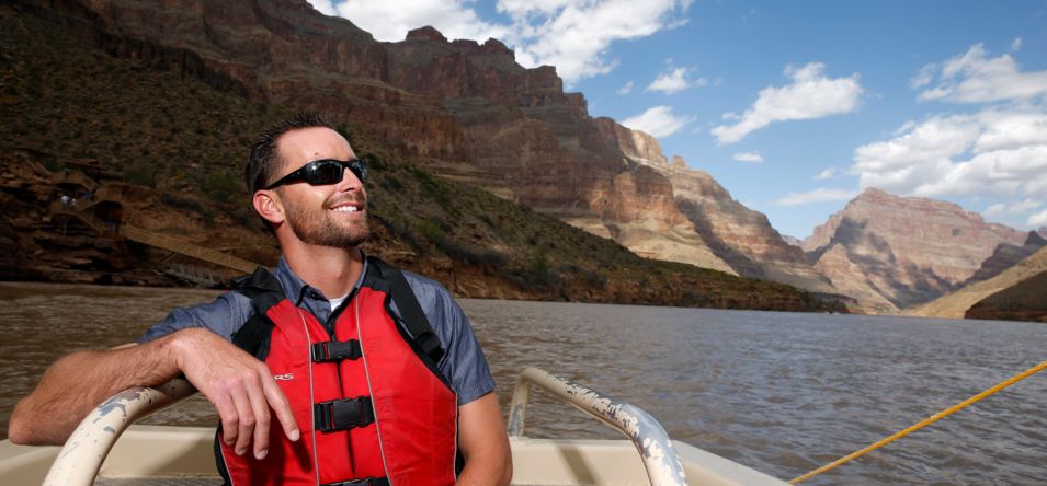 a man smiles while riding on a boat along the Colorado River at the bottom of the Grand Canyon