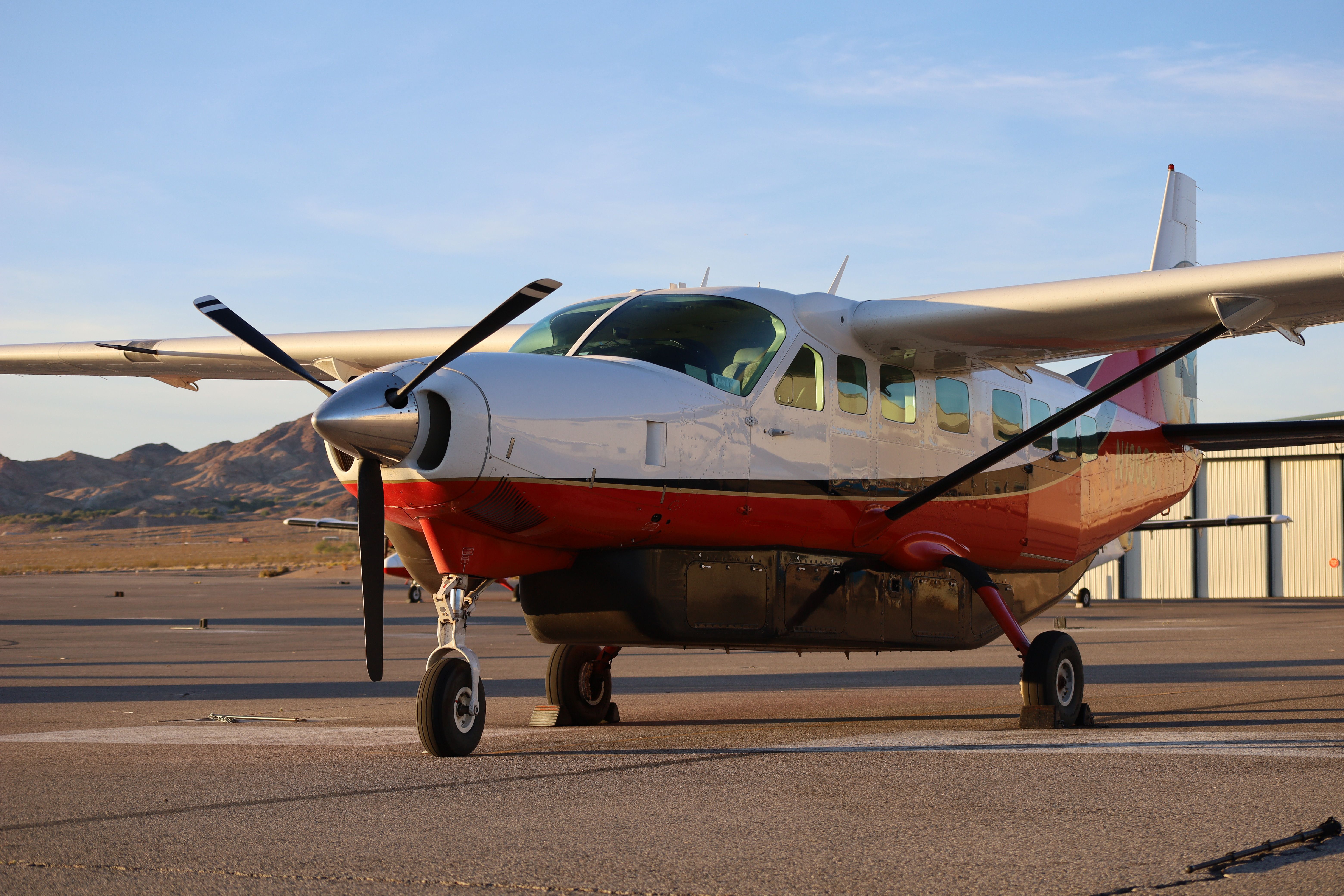 A Cessna Caravan airplane rests at the Boulder City, NV air terminal tarmac during sunset