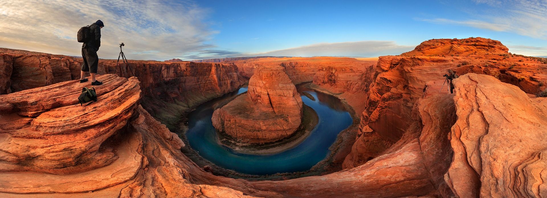 A photographer stands above the bright orange walls and blue waters of Horseshoe Bend