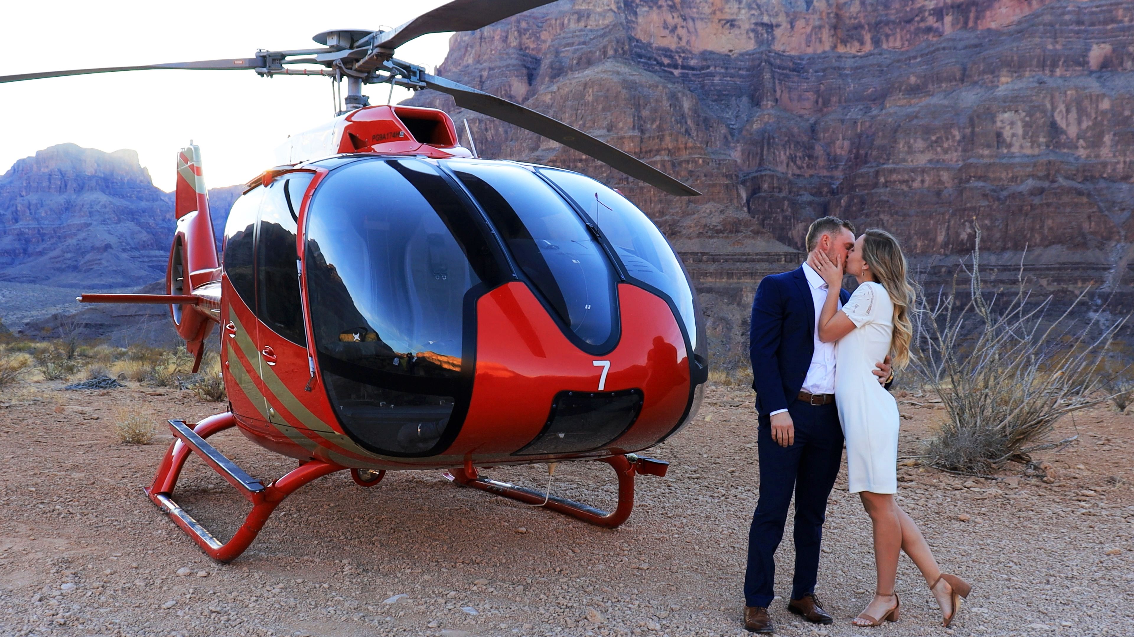 a couple kisses in front of a helicopter landed on the bottom of the Grand Canyon West
