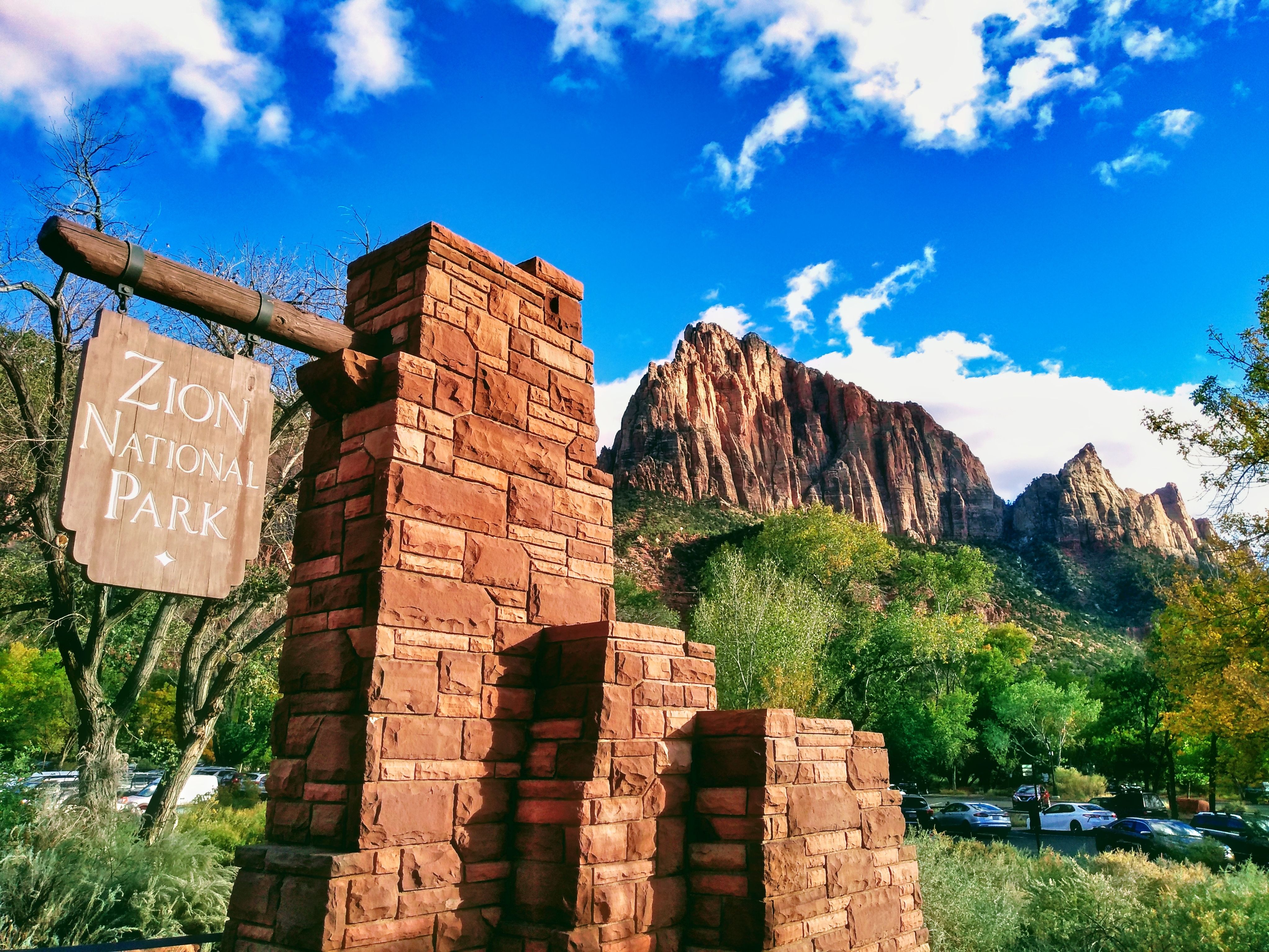 A brick structure displaying the entry sign for Zion National Park seen in front of a large mountain