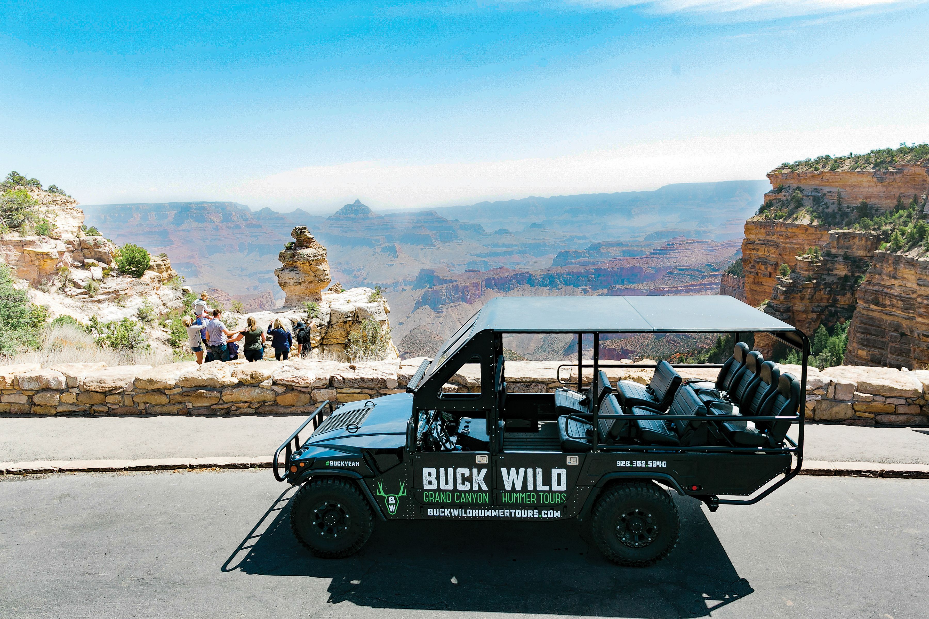 Several guests at the Grand Canyon stand at a viewpoint behind a Hummer vehicle